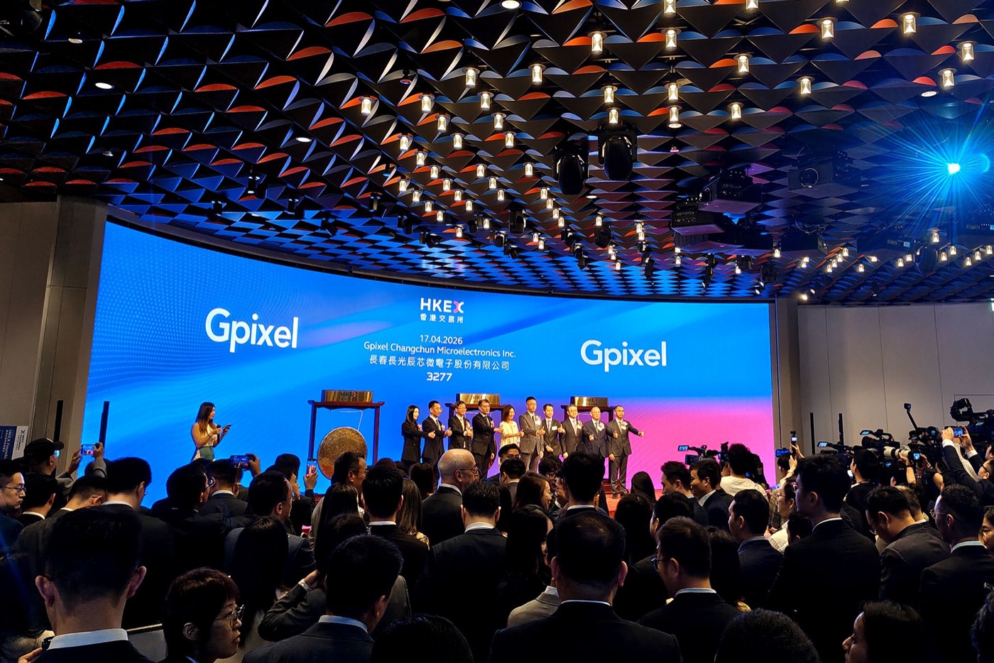 An HKEX listing ceremony in progress, the curved hall screen showing the newly listed company and its ticker